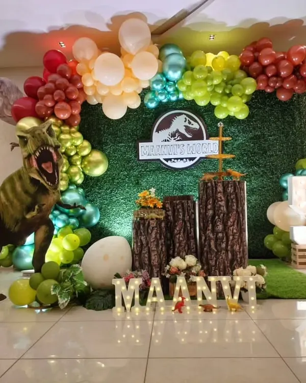 A thrilling Jurassic World theme with a large T-Rex prop, a grass wall backdrop, and tree stump pedestals.