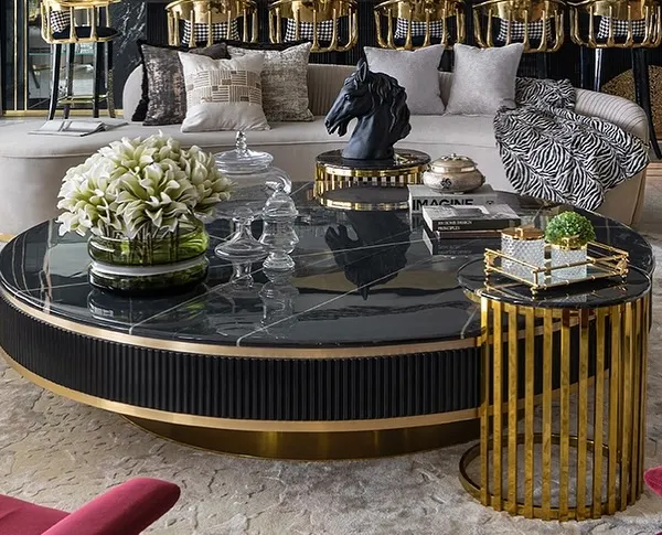 A close-up of a custom-designed living room set. The fluted black base of the coffee table, topped with black marble, contrasts with the gold-caged side table and the plush, neutral-toned sofa.