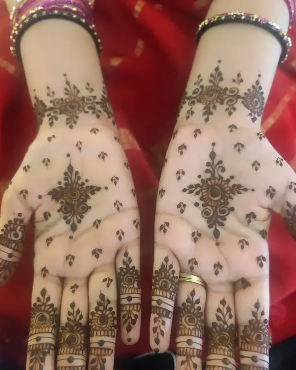 A lovely example of a minimal bangle-length design. The pattern features a central star-like mandala on the palm with delicate finger details and small motifs scattered across the hand.