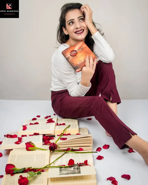 A conceptual shoot titled 'Bittersweet Memories'. The model sits among scattered books and rose petals, holding a book with a wistful expression, creating a scene that evokes romance and nostalgia.