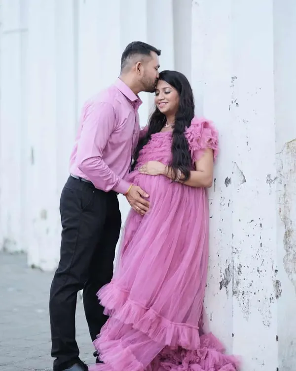 A sweet forehead kiss and a perfectly coordinated look. The mom-to-be is glowing in a pink ruffled tulle gown, while her partner's matching shirt ties their couple's maternity look together beautifully.