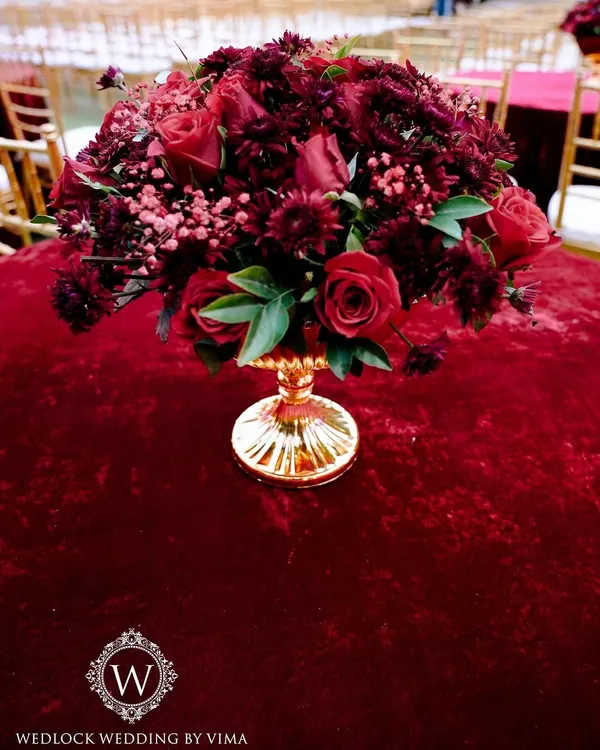 A luxurious centerpiece featuring a bouquet of deep red roses in a golden vase. This classic and elegant detail was part of a glamorous red-themed reception.