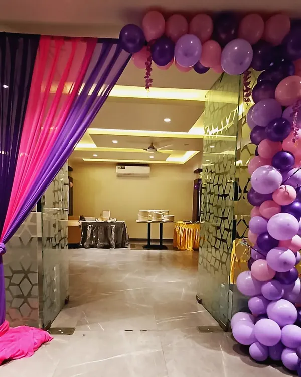 A simple yet elegant entrance decor. The combination of purple and pink drapes with a matching balloon arch creates a welcoming and festive entryway for any party.