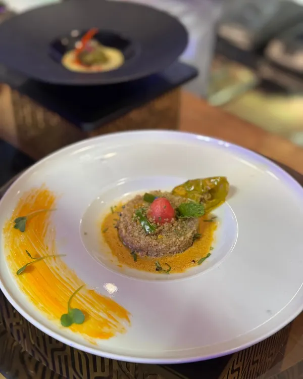A minimalist canvas for maximum taste. This dish features a quinoa base with a vibrant sauce, garnished with microgreens and pickled chili, showcasing our belief that food should be both beautiful and delicious.