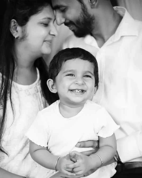 A joyful black and white family portrait, with the baby's bright smile at the center of his parents' loving gaze.