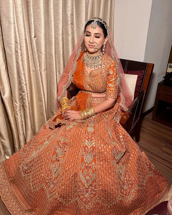 A beautiful bride looking radiant in our heavily embroidered orange bridal lehenga for her big day.