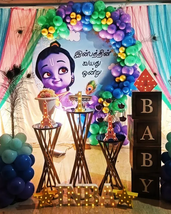 A beautiful and traditional theme featuring Little Krishna for a first birthday. The decor uses peacock feathers and a vibrant color palette to create a divine and celebratory atmosphere.