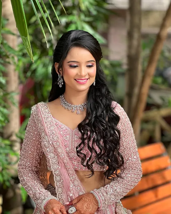 A beautiful engagement bride in a baby pink lehenga. She is wearing a delicate, single-line diamond necklace with matching earrings, perfect for a subtle yet elegant look.