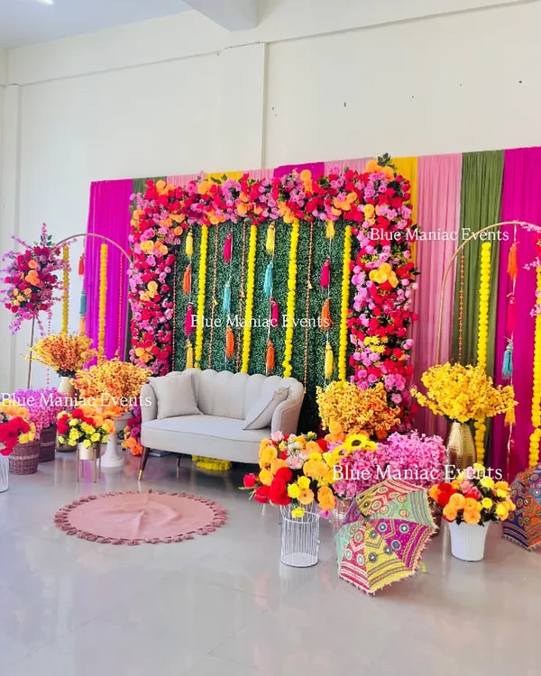 A grand and colorful Mehendi setup, featuring a vibrant floral frame, a green wall with tassels, and an abundance of bright flowers. This decor is perfect for making a statement.