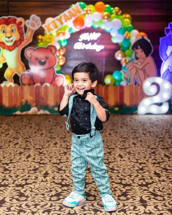 The birthday boy, turning two, strikes a cool pose in front of his jungle-themed party decorations.