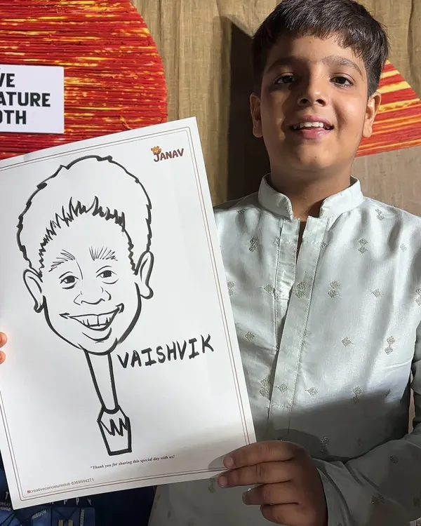 A young boy in traditional wear proudly holds up his black and white ink caricature. The simple, bold lines really capture his cheerful expression.