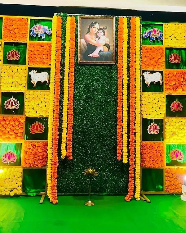 A vibrant and creative backdrop for a Sreemantham. This wall is made of fresh marigolds in a checkerboard pattern, with traditional motifs and a portrait at the center.