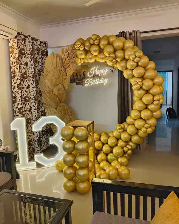 A stylish and modern setup for a 13th birthday party. This decoration features a large marquee number '13', a circular balloon arch in metallic gold, and dried pampas grass for a trendy, bohemian touch.