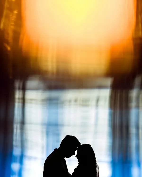 An abstract and artistic silhouette of a couple. The vibrant, warm colors in the background create a painterly effect, focusing on the intimate connection in their outline.