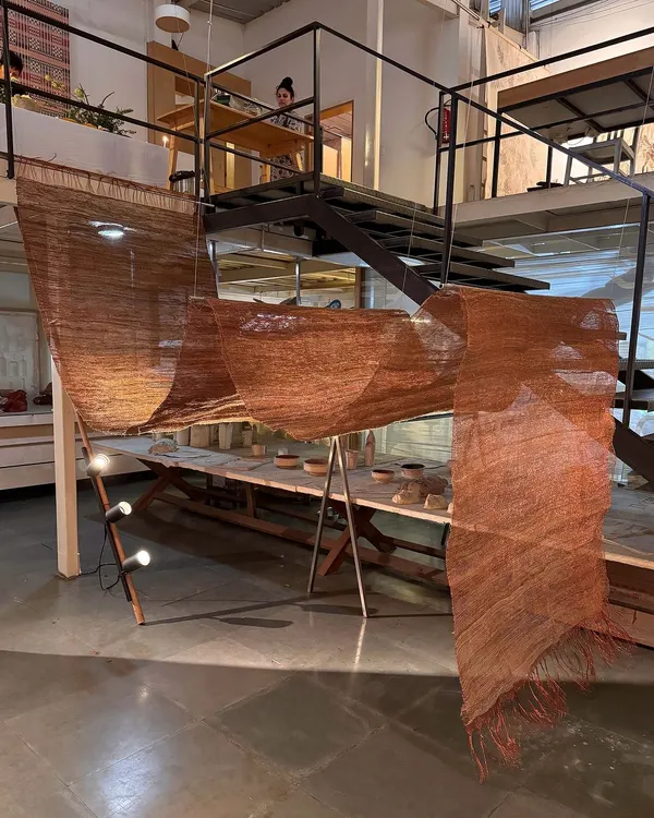 A free-flowing woven sculpture from our 'Cu+Fibers' exhibition, created in our studio. This piece is a play of hand-spun and machine-made fibers like hemp, jute, and copper, manipulated and formed to catch the light.