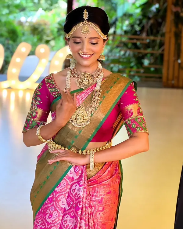 A beautiful muhurtham look featuring a traditional temple jewellery set on a pink and green patola saree. The matha patti and layered necklaces create a classic South Indian bridal look.