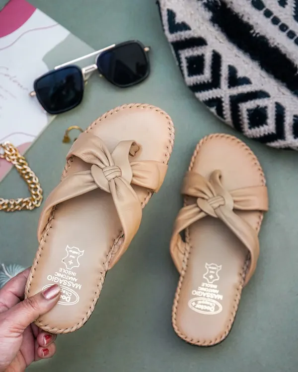 A lifestyle shot of a hand holding a pair of beige sandals, with sunglasses and a bag as props. This creates a 'get ready with me' vibe that is very popular on social media.