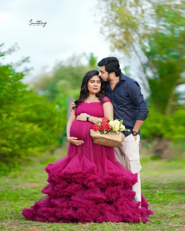 An intimate outdoor moment with the couple dressed in a stunning magenta gown. The natural greenery and the tender kiss create a romantic and unforgettable portrait.