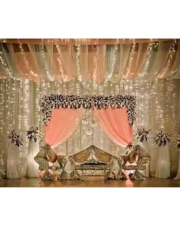 A classic reception stage featuring a beautiful floral arch, delicate pink draping, and a backdrop of twinkling fairy lights. This design creates a romantic and elegant focal point for any wedding or mehendi ceremony.