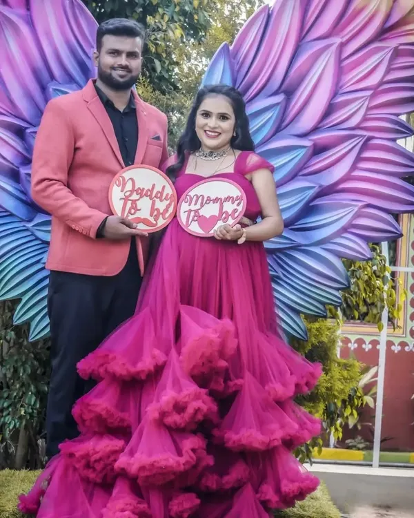 A fun and imaginative shot using the angel wings backdrop. The couple holds "Daddy To Be" and "Mommy To Be" signs, creating a playful and memorable portrait.