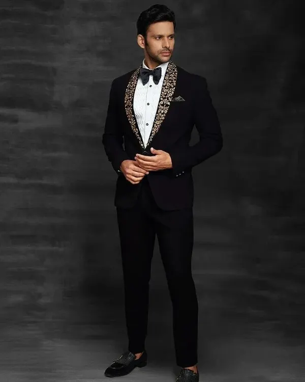 This black tuxedo features a unique embroidered shawl lapel, giving a modern twist to a classic style. It's the perfect outfit for a groom who wants to look sharp and sophisticated at his reception.