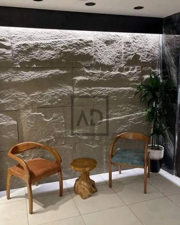 This finished accent wall in a waiting area uses PU stone panels with integrated strip lighting at the top. The light grazes the surface, highlighting the rugged texture and creating a warm, inviting atmosphere.