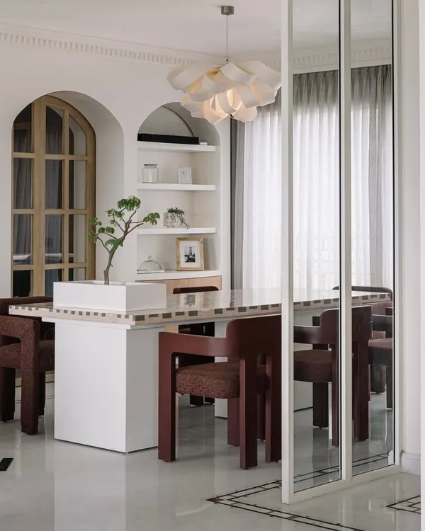 An overview of the dining area in Eden House, a lush penthouse in Bengaluru. The design combines modern lines with whimsical details, like the floral-inspired chandelier and arched shelving.