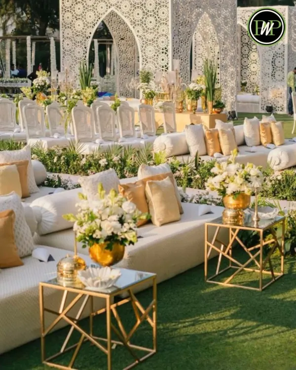 A luxurious outdoor seating lounge with pristine white sofas, intricate Moroccan-style backdrops, and elegant gold and glass tables. This setup is perfect for a chic, modern wedding.