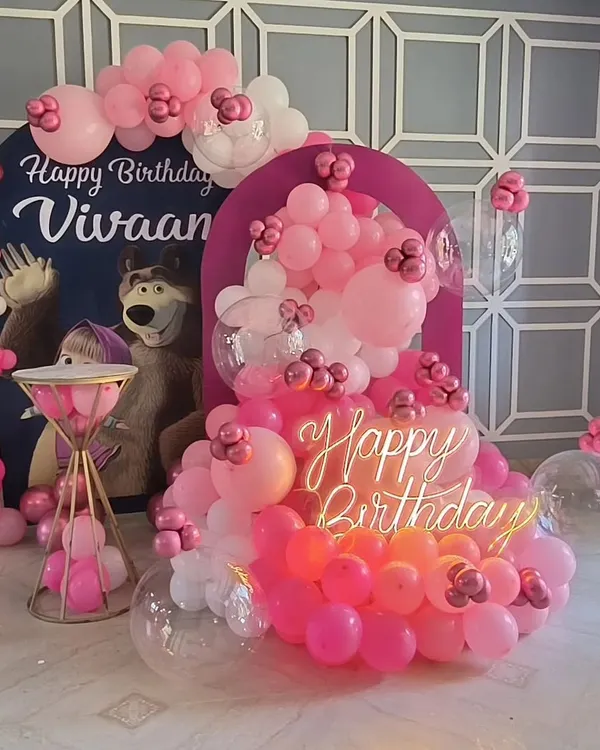 A fun Masha and the Bear theme featuring character cutouts against a custom arch backdrop. The pink balloon cascade, clear bubble balloons, and a 'Happy Birthday' neon sign make this a delightful setup for a young child's party.