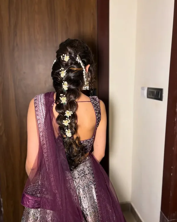 A stunning view of a voluminous braided hairstyle, adorned with delicate white flowers and a large pearl hair accessory. This is a perfect choice for a sangeet or reception.
