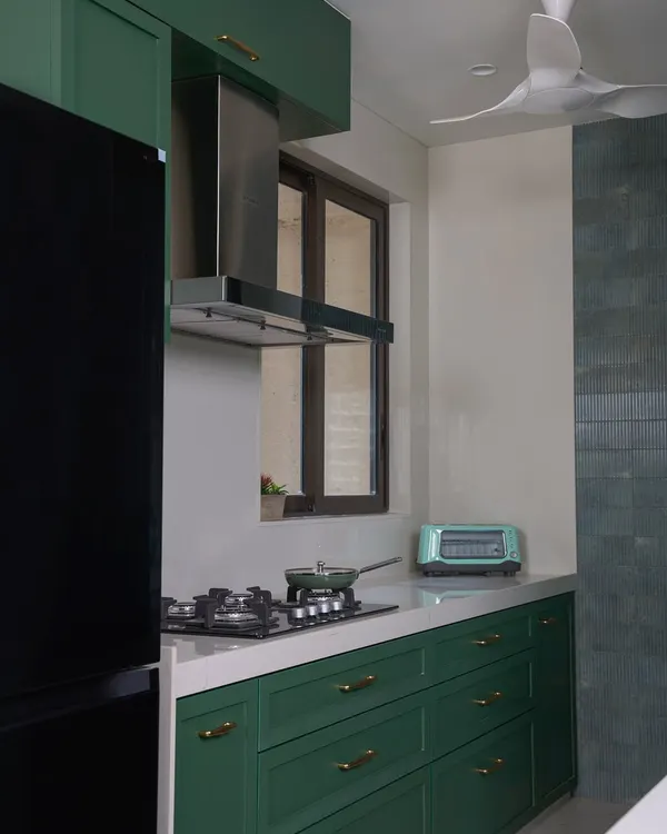 This stunning green kitchen is finished with premium quality laminate and full-body tiles. A sleek Italian marble breakfast counter seamlessly connects the kitchen and living room, serving as a stylish focal point.