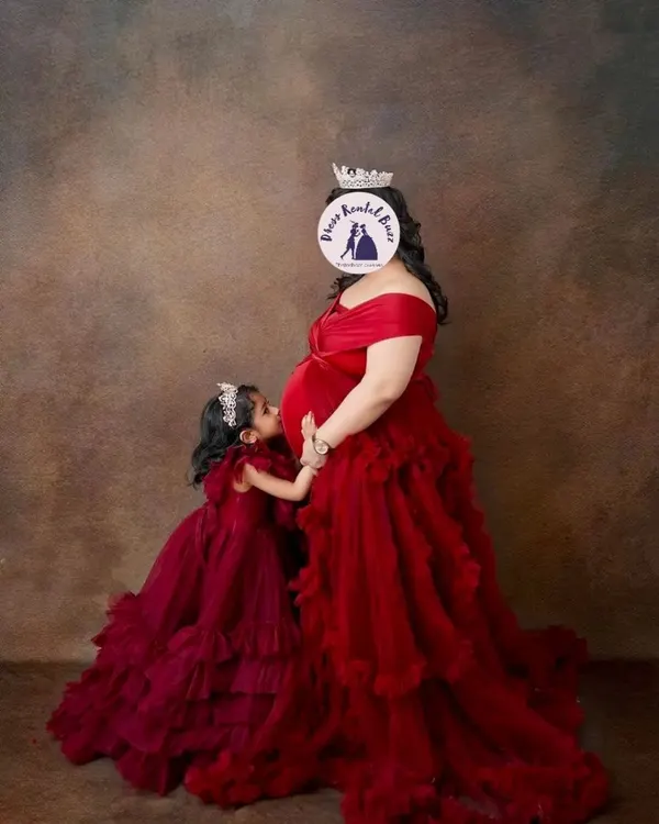 A heartwarming portrait of a mother and daughter in matching burgundy ruffled gowns. Including older siblings is a wonderful way to celebrate the new addition to your family.