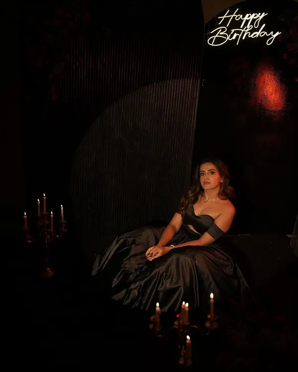 A sophisticated and dramatic birthday photoshoot. The dark, moody decor with minimalist backdrops, candlelight, and a neon sign creates a stunning, high-fashion look.