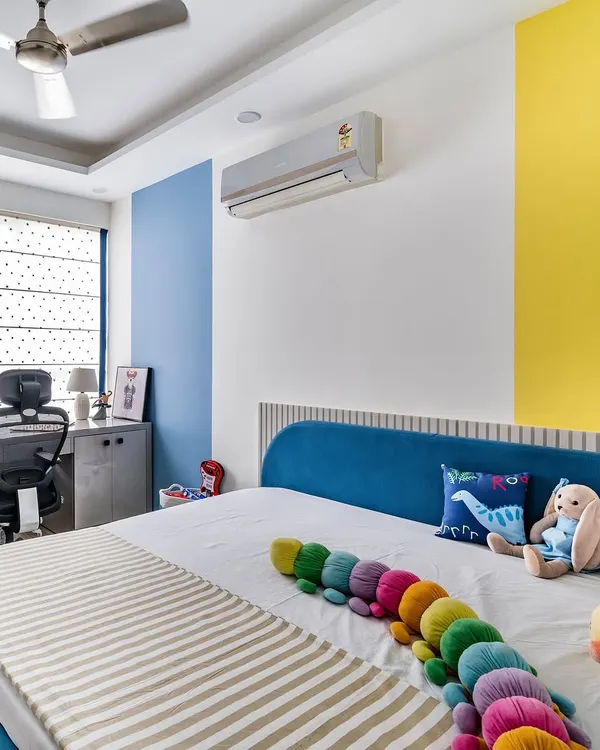 A vibrant and cheerful kid's room featuring a custom blue bed, a compact study desk, and bold color-blocked walls in yellow and blue to stimulate creativity.
