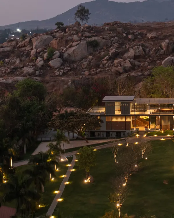 An aerial view of 'The Earth' Experience Centre at dusk, showing how the building and its landscape lighting are thoughtfully integrated into the natural topography of the Nandi Hills.
