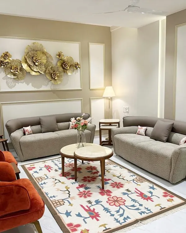 In this South Mumbai living room, I curated a harmonious blend of elegance and vibrancy. The space features a custom floral rug, terracotta-colored armchairs, and a striking 3D metal flower installation, all balanced by neutral sofas and wall paneling.