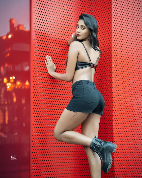 An edgy urban fashion shot using a vibrant red perforated wall as a graphic backdrop. The contrast between the red wall and the black outfit creates a bold and modern look.