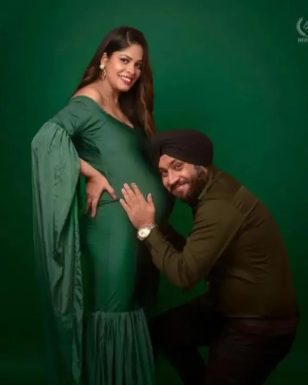 A partner lovingly listens to the baby bump in this studio shot. The mom-to-be is wearing a beautiful bottle green mermaid gown with cape sleeves, creating an intimate and stylish portrait.