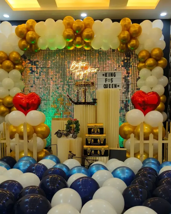 This "Better Together" setup is perfect for anniversaries or romantic celebrations. It features a stunning arch of gold and white balloons, a shimmering backdrop, and red heart accents to symbolize love.