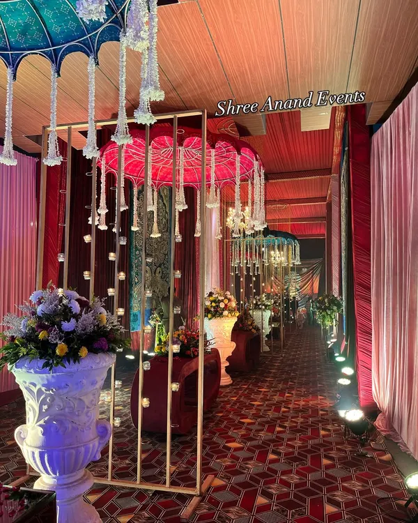 A welcoming pathway for guests, lined with traditional Rajasthani umbrellas, candle-lit partitions, and large floral urns, creating a warm and inviting atmosphere.