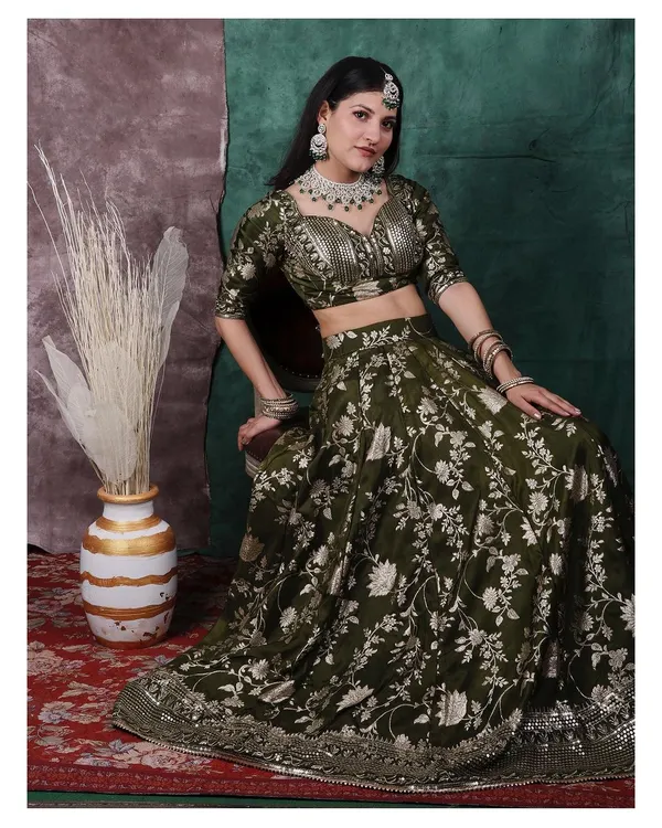 A full portrait showcasing a stunning olive green lehenga. The studio lighting is set to bring out the silver floral embroidery and the sparkle of the diamond jewellery, creating a look of pure royalty inspired by classic period dramas.