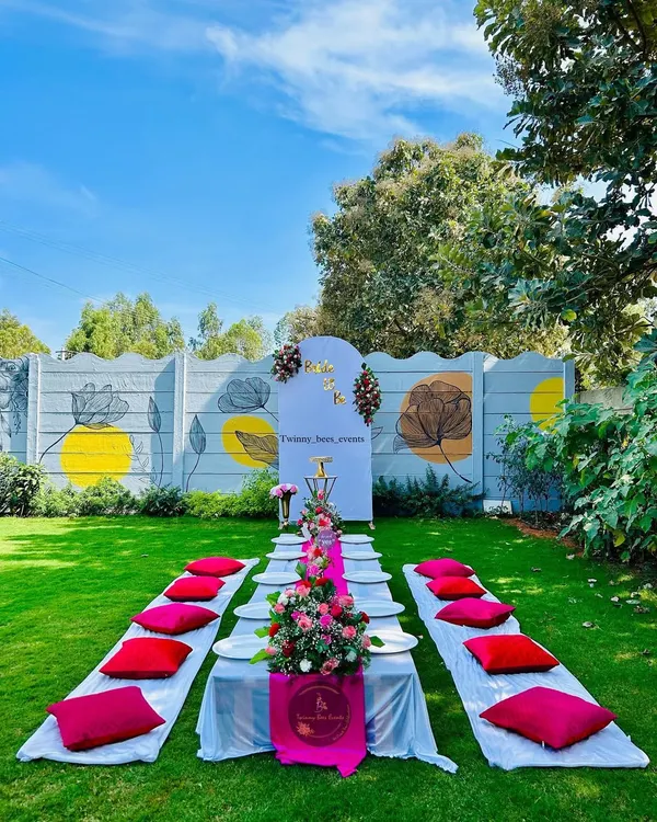 A beautiful outdoor picnic-style setup for a "Bride to be" party. We arranged a low table with a floral runner and comfortable floor seating on a lush green lawn for a relaxed and stylish celebration.