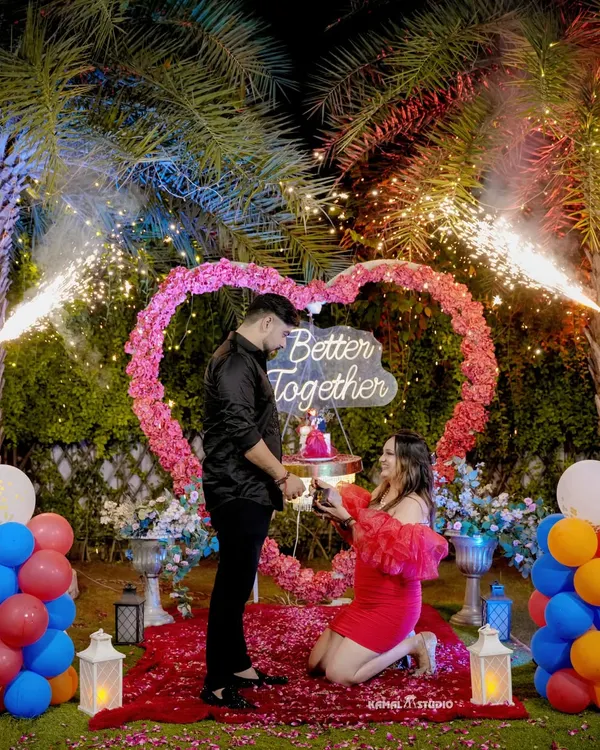 The pinnacle of a surprise proposal. The moment of the question, complete with fireworks, a heart-shaped floral arch, and a path of rose petals.