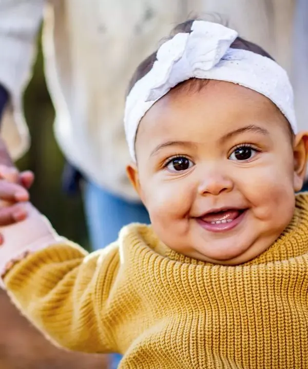 That big, gummy smile is just the best. This close-up captures the pure happiness of a baby who is learning to stand with a little help.