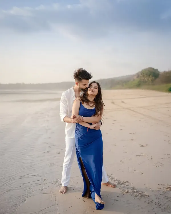 A gentle embrace on the sand, with the soft light of the setting sun creating a warm glow. This is a classic romantic beach portrait, focusing on the connection and tenderness between the couple.