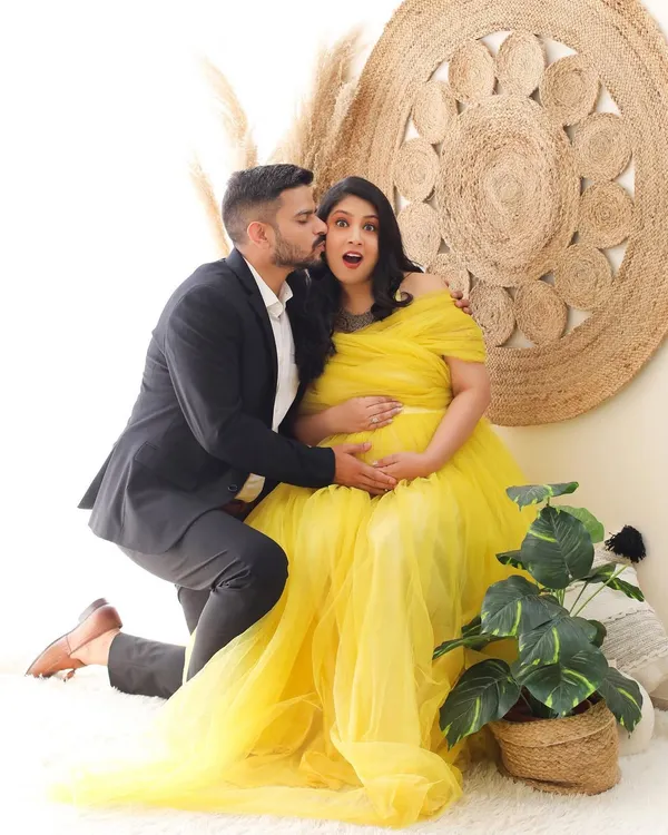 A playful and candid moment captured during a maternity session. The bright yellow gown and bohemian-style backdrop create a cheerful and sunny atmosphere, perfect for celebrating this happy time.