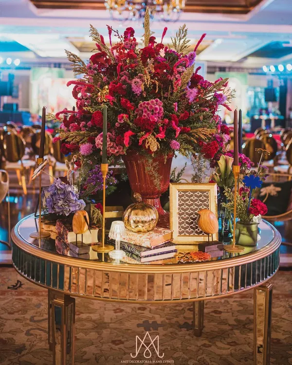 A stunning centerpiece for a contemporary sangeet. I love combining lush florals with unique decorative objects like this mirrored table, patterned books, and a golden pumpkin.