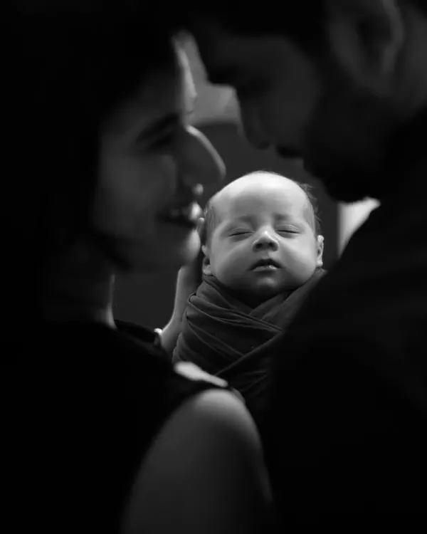 An intimate black and white portrait focusing on the tender moment between new parents and their sleeping newborn. This is pure love.