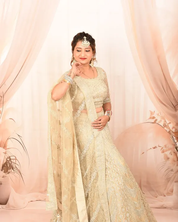 An elegant studio portrait featuring a woman in a beautiful cream-colored lehenga. The soft, draped background adds a touch of sophistication.
