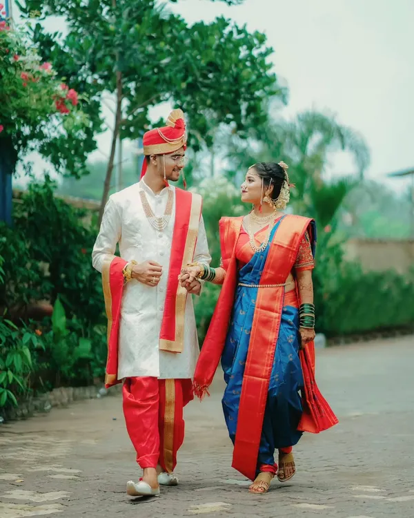 A Maharashtrian couple takes a walk together, hand in hand. The groom in his sherwani and the bride in her traditional blue and red Navvari saree create a picture of classic elegance.